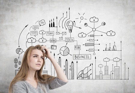 Close up of a blonde businesswoman scratching her head and thinking near a concrete wall with a business plan sketch on it.の写真素材