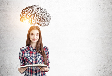 Portrait of a pensive young businesswoman in a shirt standing near a concrete wall with a brain sketch on it. Mock up toned imageの写真素材