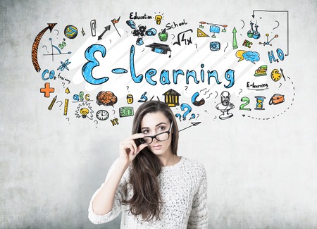 Young woman with dark long hair is wearing a white sweater and holding her glasses with a thick frame. She is looking to the distance while standing near a concrete wall with an e learning sketchの写真素材