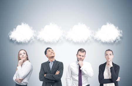 Members of a diverse business team are standing near a gray wall and thinking. There are thought clouds above their heads. Mock upの写真素材