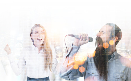 Close up of a bearded man singing in a microphone and a blonde woman cheering him. A cityscape. Toned image double exposureの写真素材