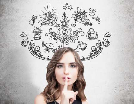 Close up of a young woman making a hush sign and standing near a man with a megaphone near a concrete wall with wedding icons on it.の写真素材