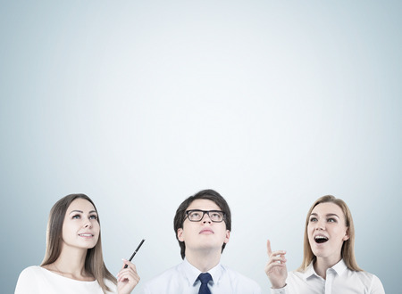 Group of young people in white clothes including a young guy in glasses and two motivated blonde women are standing near a gray wall, mock upの写真素材