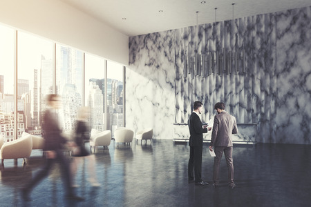 Side view of a marble reception desk standing in a marble wall office lobby with a white armchair in the waiting area. People 3d rendering mock up toned imageの写真素材