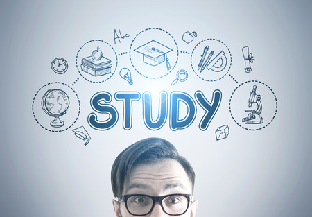 Close up of a head of a young man wearing glasses. He is standing near a gray wall with a study sketch drawn on it. Toned imageの写真素材