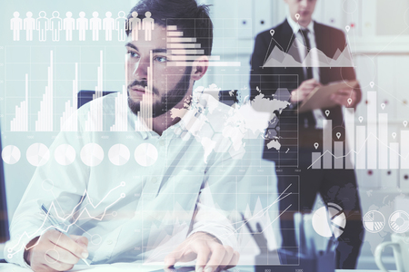 Two young and attractive businessmen working in a white office. Graphs and infographics. Toned image double exposureの写真素材