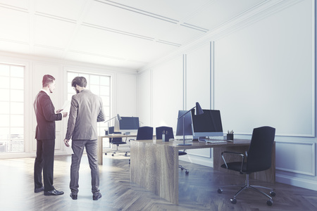Business people in a white open space office corner with a wooden floor, two large windows and wooden desks with computers on them. 3d rendering toned imageの写真素材