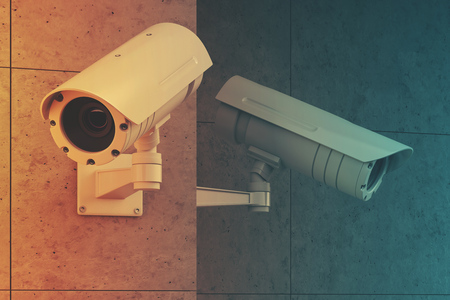 Close up of two white CCTV cameras attached to a blank gray wall outside. Concept of security and...