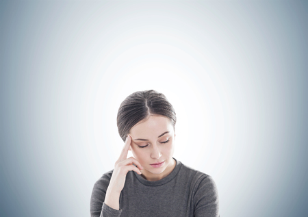 Portrait of a stressed out young woman in brown having a headache and standing with closed eyes. A gray wall background.の写真素材