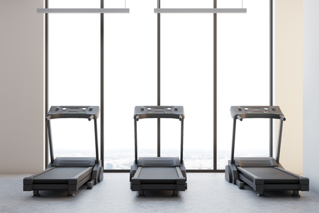 Three treadmills standing on a concrete floor in a room with panoramic windows and white walls. 3d rendering mock upの写真素材