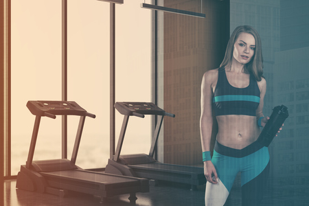 Two treadmills standing on a concrete floor in a room corner with panoramic windows and gray walls. Attractive woman. 3d rendering mock up double exposure toned imageの写真素材