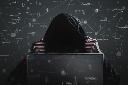 Unrecognizable African American man in a black hoodie looking at his laptop screen. Black background...
