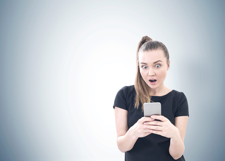 Portrait of a young astonished woman with a ponytail wearing a black T shirt and looking at her...