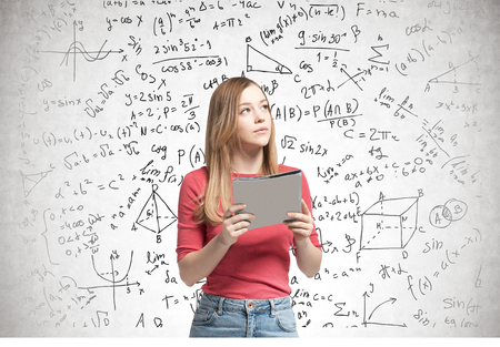 Young blonde woman wearing a pink sweater and jeans and holding a folder is looking sideways. A...