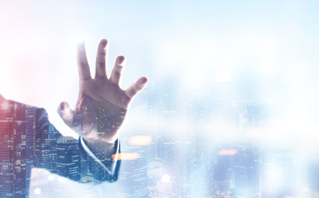 Hand of a businessman wearing a suit a blurred cityscape background. Double exposure toned image mock upの写真素材