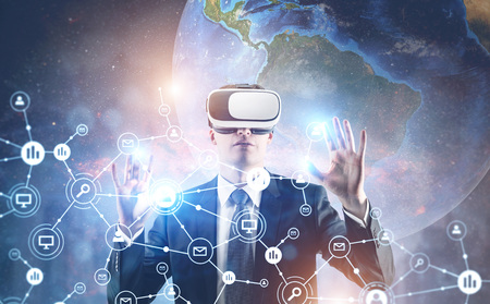 Portrait of a young businessman wearing a suit and VR glasses and interacting with what he sees. A...