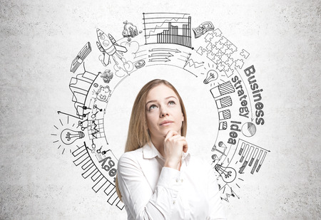 Dreamy blonde businesswoman standing near a concrete wall with a round business plan sketch on it.の写真素材