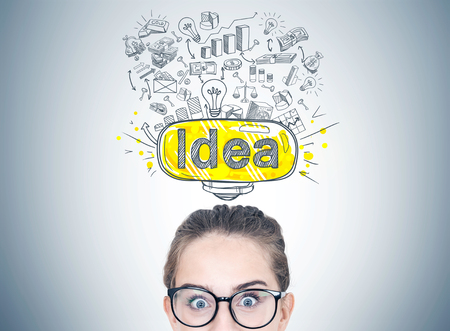 Head of an astonished young woman wearing glasses. A gray wall background with a colorful idea sketchの写真素材