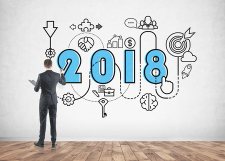 Rear view of a businessman drawing a colorful large 2018 business plan sketch on a concrete wall. Concept of creativity and tactics in businessの写真素材