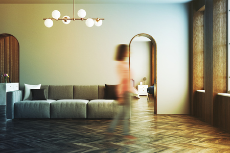 Modern gray living room interior with a gray sofa, narrow doorways and a wooden floor. A woman in 3d rendering mock up toned image blurredの写真素材