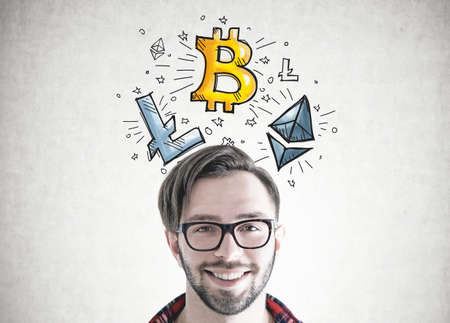 Head and shoulders portrait of a smiling hipster man wearing glasses and a trendy haircut. A concrete wall background with a cryptocurrency sketch. Bitcoinの写真素材