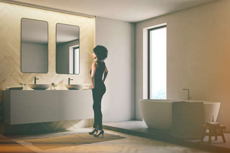 White and light wooden bathroom interior with a white tub, and a double sink. Narrow tall windows An African American woman. 3d rendering mock up toned imageの写真素材