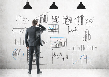 Rear view of a thoughtful well dressed businessman scratching his head. Concept of confusion and a helping hand. Graphs drawn on a concrete wallの写真素材