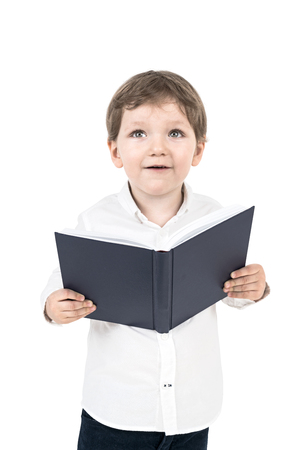 Portrait of a cute little boy in a white shirt holding an open book and looking upwards. An isolated portraitの写真素材