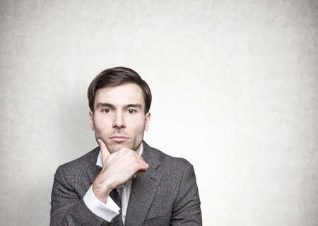Head and shoulders portrait of a thoughtful young businessman with dark hair looking at the camera....