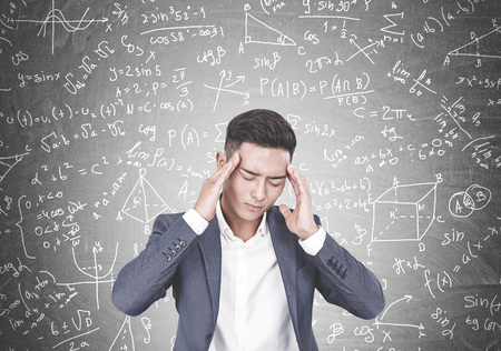 Young Asian businessman wearing a suit and a white shirt having a headache. A chalkboard background...