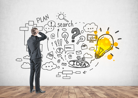 Rear view of a confused businessman scratching his head and thinking. Start up idea sketch drawn on a concrete wall.の写真素材