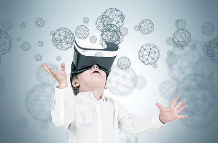 Cute little boy in a white shirt and jeans wearing VR glasses and looking upwards. A gray background with polygons and little orbs, double exposure mock upの写真素材