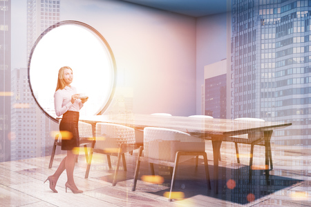Gray dining room corner with a concrete floor, a long table with beige chairs standing near it and a round window. A blonde woman 3d rendering mock up toned image double exposureの写真素材