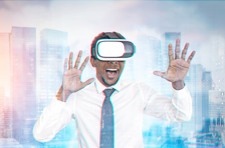 Happy young African American businessman wearing a suit and VR glasses. Concept of the future technology. A modern city background. Toned image double exposureの写真素材