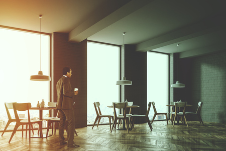 Corner of a gray brick loft cafe with a wooden floor, round tables and wooden chairs. A man with a coffee 3d rendering mock up toned image double exposureの写真素材