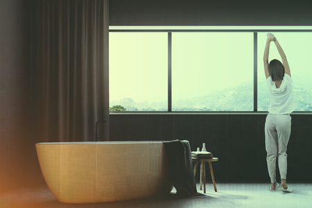 Gray bathroom interior with a concrete floor, a large window with gray curtains, and a white bathtub. A woman 3d rendering toned image double exposureの写真素材