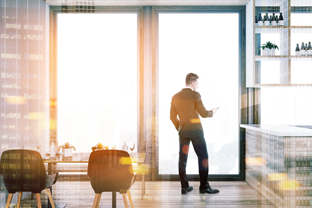 Businessman looking at his phone in a loft luxury restaurant interior with a wooden floor, a set table with black chairs near the window and a bar. 3d rendering mockup toned image double exposureの写真素材