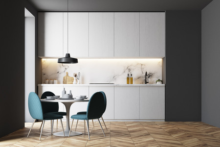 Gray kitchen interior with white countertops, a round wooden table and chairs standing around it. A...