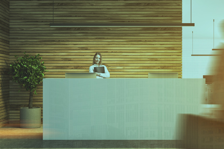 Blonde businesswoman near a long white reception table in a wooden wall company lobby with a concrete floor. A tree in a pot in the corner. 3d rendering mock up toned image double exposure blurredの写真素材