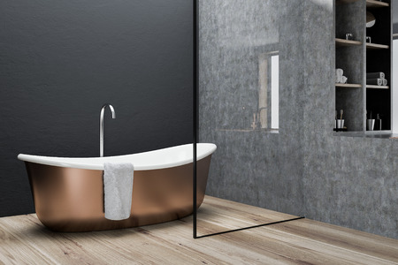 Bronze bathtub with a towel hanging on it standing on a concrete floor of a minimalistic gray wall...