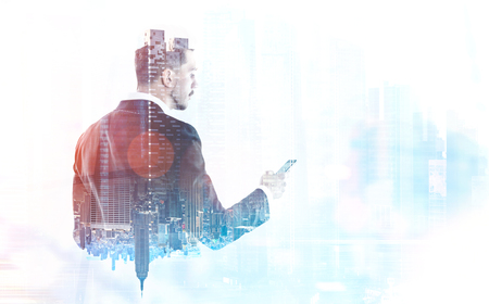 Rear view of a young businessman looking at his smartphone screen. A blurred foggy cityscape. Concept of communication in a modern society and business. Toned image double exposure mock up Rear view of a young businessman looking at his smartphone screen. A blurred foggy cityscape. Concept of communication in a modern society and business. Toned image double exposure mock up