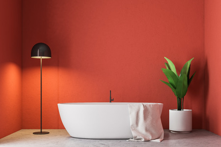 Minimalistic red bathroom interior with a white bathtub, a towel hanging on it, a potted tree and a lamp in the corner. 3d rendering mock upの写真素材