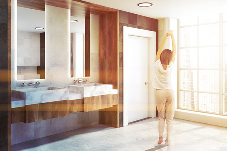 Double bathroom sink with two narrow tall framed mirrors hanging above it in a classic bathroom with a wooden wall. A side view. A woman 3d rendering toned imageの写真素材