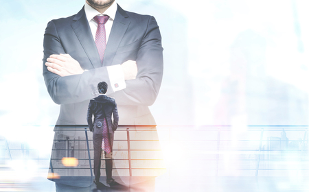 Rear view of a businessman against a crossed armed unrecognizable businessman figure and a foggy cityscape. Concept of leadership. Toned image double exposure mock upの写真素材