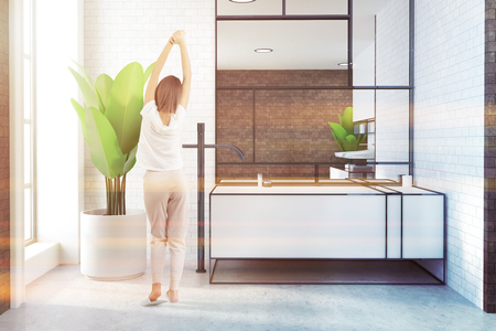White sink in a white brick loft bathroom interior with a white floor and a potted plant. A large mirror. A woman. 3d rendering mock up toned imageの写真素材