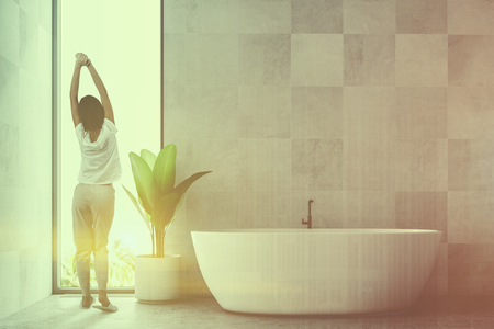 White wooden tile bathroom interior with a concrete floor and a white bathtub standing near a potted plant. A loft window and a woman. 3d rendering mock up toned image double exposureの写真素材