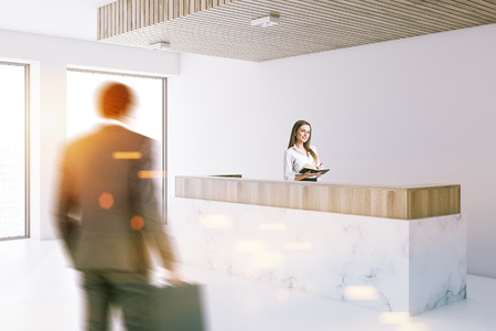 Marble and wooden reception desk standing in a modern office lobby with a white floor and walls and panoramic windows. People. 3d rendering mock up toned image blurredの写真素材