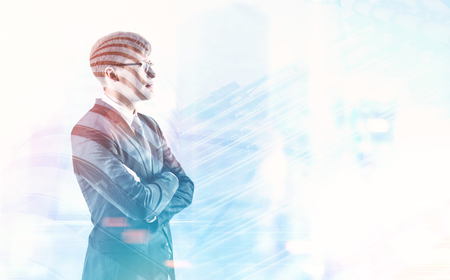 Side view of a young handsome businessman wearing glasses and a gray suit and standing with crossed arms against a cityscape. Leadership concept. Toned image double exposure mock up.の写真素材