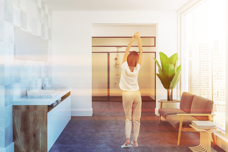 Woman in a white tile spacious luxury bathroom interior with a concrete floor, a wooden double vessel sink and a narrow mirror hanging above it. A couch. 3d rendering mock up toned imageの写真素材