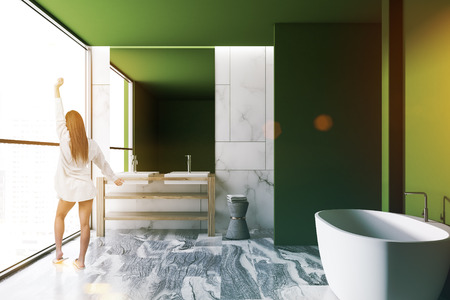 Woman in a loft green wall luxury bathroom interior with a gray marble floor, a white bathtub, and a double vessel sink. 3d rendering mock up toned imageの写真素材